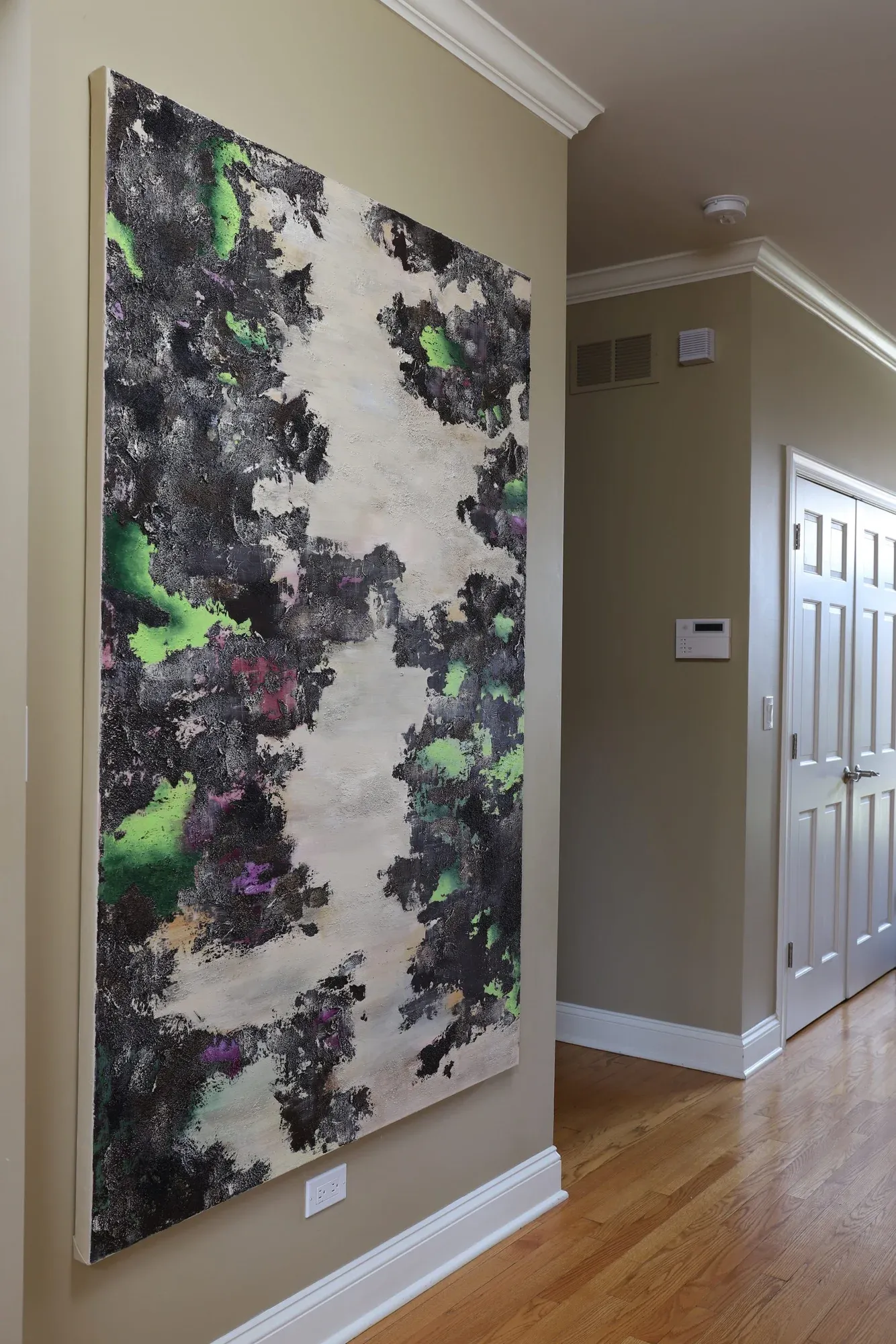 Large abstract painting in purple, green, and black hung in a hallway