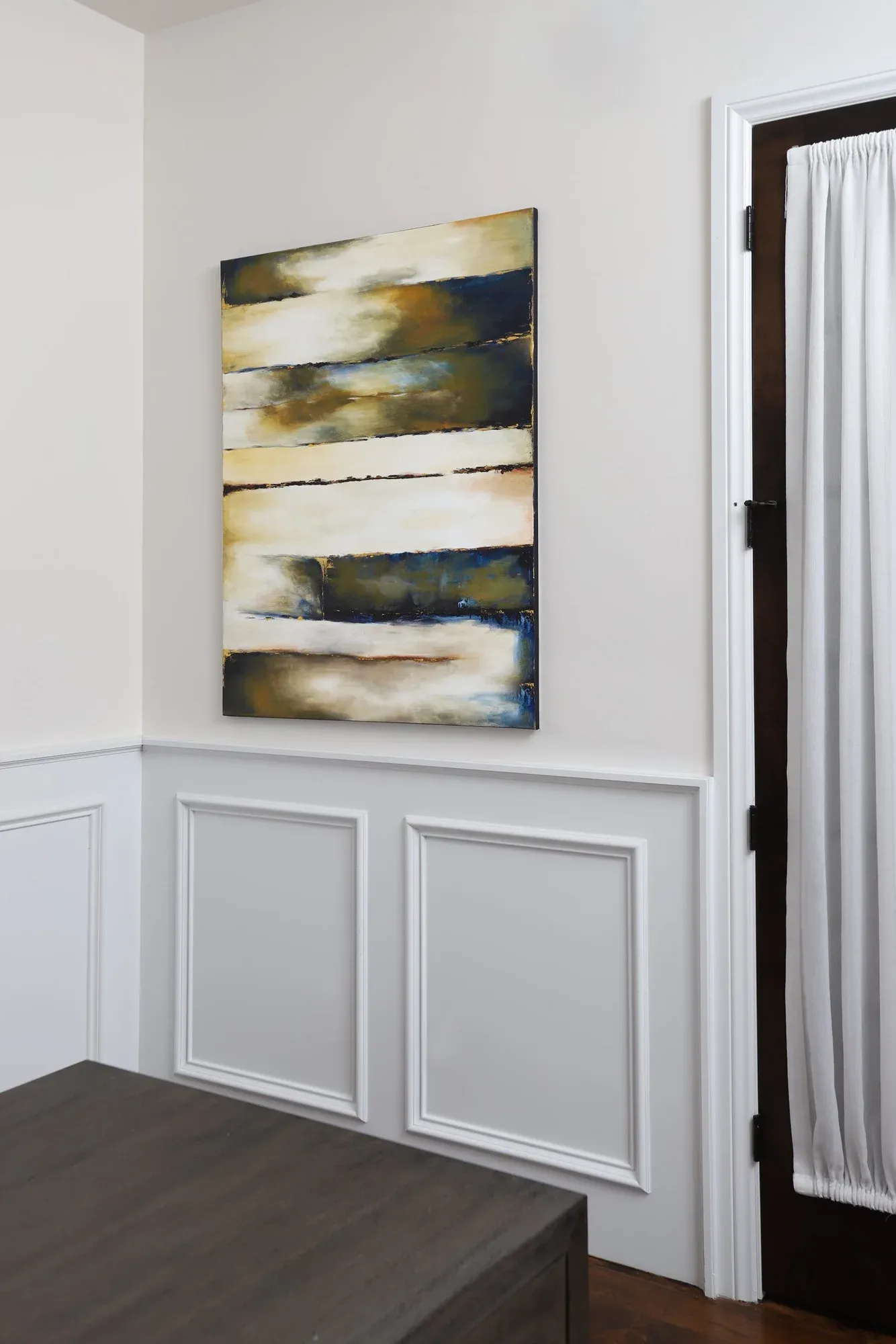 Abstract painting in blue, gold, and white above wood wainscoting