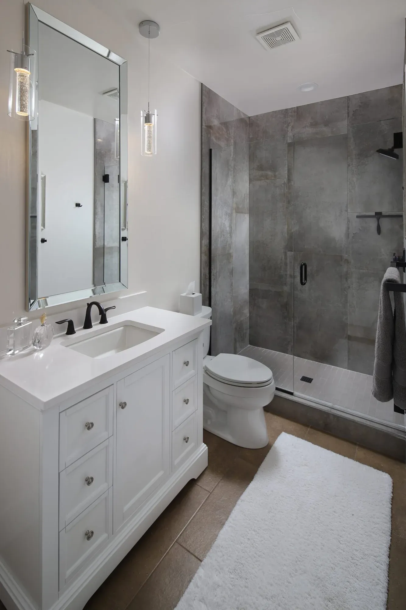 Bright bathroom with a white vanity, glass-enclosed shower, and gray tile