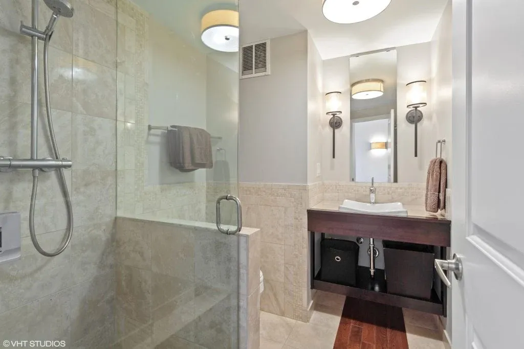 Bathroom with a glass shower, pale stone tile, and a wood vanity