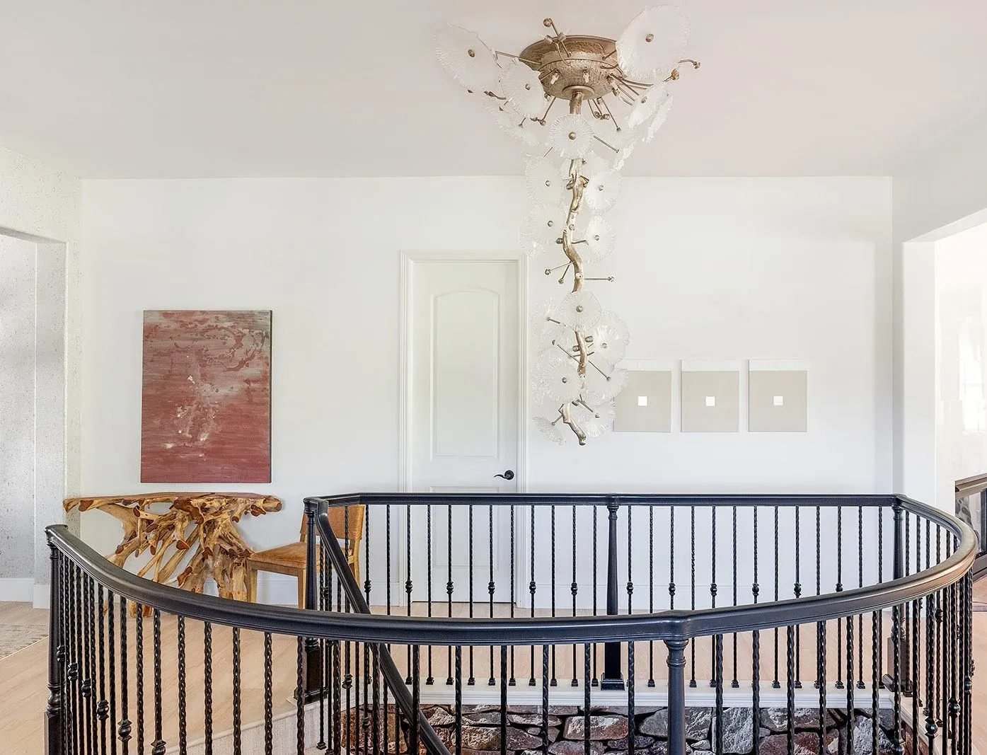 Curved staircase with dark balusters, a crystal chandelier, and a large pink painting