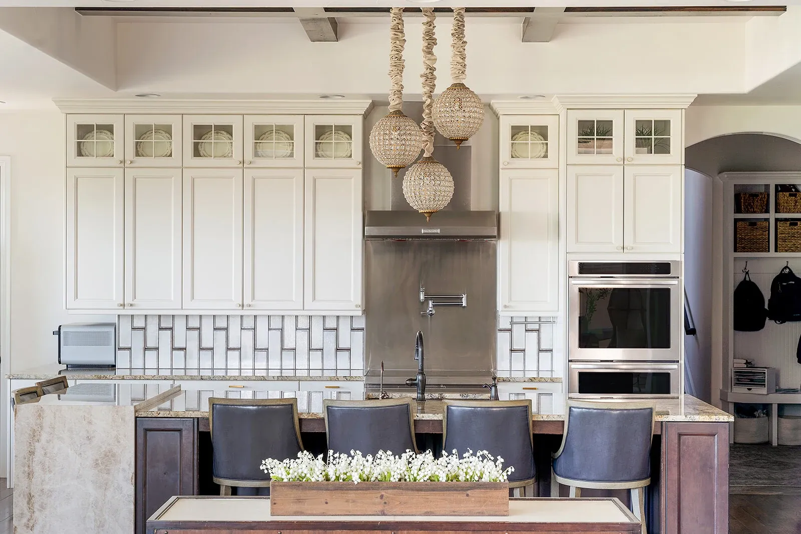 White kitchen with a sculptural metal range hood, patterned backsplash, and island seating